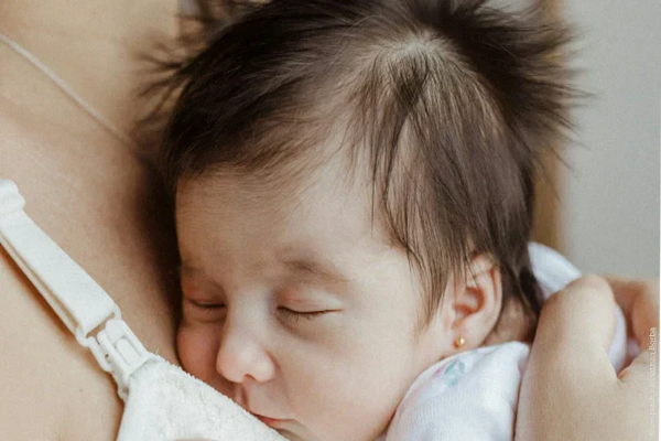 Eine Frau hält ihr schlafendes Baby liebevoll an der Brust. | © Jonathan Borba